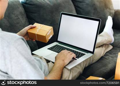 Asian man hold a delivery box for shipping and are using a laptop blank screen.