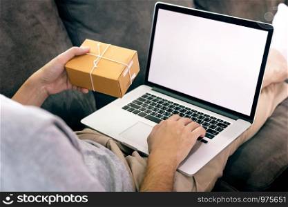 Asian man hold a delivery box for shipping and are using a laptop blank screen.