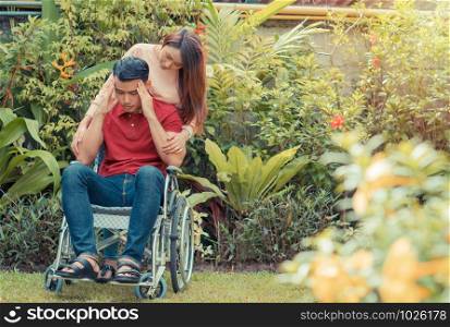 Asian Man in a wheelchair and Unhappy and painful. A woman standing behind the wheelchair and is encouraging her husband, whose feet hurt his leg due to an accident. Concept of caring and support