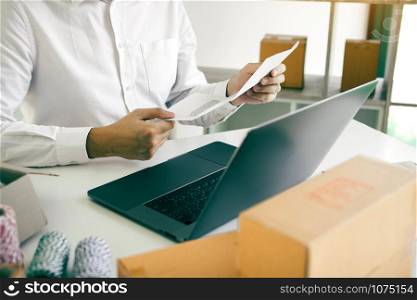 Asian man is holding a piece of paper to check the list of customer orders at his desk.