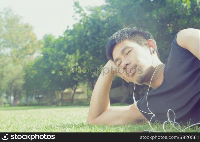 Asian man laying down in garden listening to music with vintage filter
