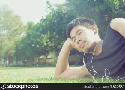 Asian man laying down in garden listening to music with vintage filter