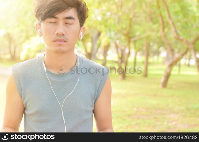 Asian man listening music with his smartphone in park