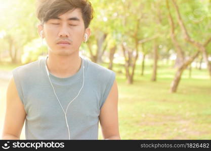 Asian man listening music with his smartphone in park