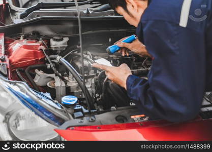 Asian Man mechanic inspection Shine a torch car engine checking bug in engine from application smartphone.Red car for service maintenance insurance with car engine.for transport automobile automotive auto repair car