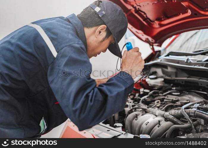 Asian Man mechanic inspection Shine a torch car engine checking bug in engine.Blue car for service maintenance insurance with car engine.for transport automobile automotive