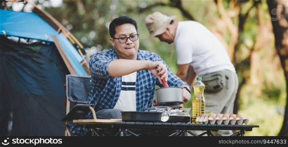 Asian man preparing pitch a tent in c&ing while the other man was preparing food. in c&ing. Cooking set front ground. Outdoor cooking, traveling, c&ing, lifestyle concept.