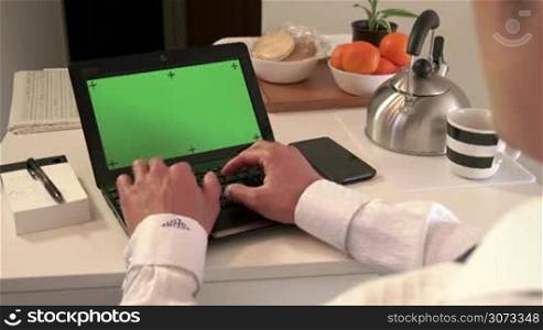 Asian man typing on keyboard, manager having breakfast, business people using laptop pc with green screen, computer monitor at home. Wi-fi technology for internet and email, lifestyle