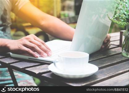 Asian man using laptop and a cup of coffee working in garden cafe or restaurant, Lifestyle and Working concept