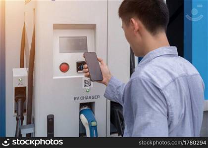 Asian Man using smartphone. EV car charger cable or electric vehicle station. Cable connected at gas station, power supply battery charging eco environment future technology energy innovation. People.