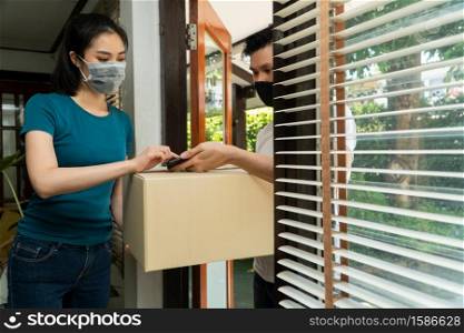 Asian man wearing a protective mask and delivering packages from grocery after online order. Woman accepting delivery boxes and Signing for the package in tablet. Concept of transportation service.