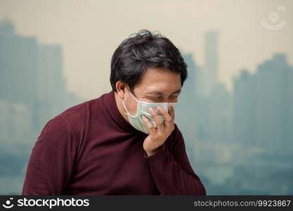 Asian man wearing the face mask against air pollution with coughing at the balcony of High Apartment which can see pollution and heavy fog over the bangkok cityscape background, healthcare concept