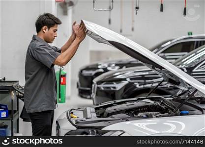 Asian mechanic Checking and Opening the car hood in maintainance service center which is a part of showroom, technician or engineer professional work for customer, car repair concept