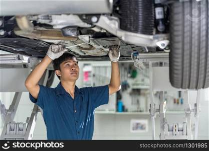 Asian mechanic repairing and light up under the car in maintainance service center which is a part of showroom, technician or engineer professional work for customer, car repair and maintain concet