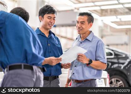 Asian Mechanic talking and showing job to the customer about repair service in maintenance service center which is a part of showroom, car repair and agreement on the job concept,