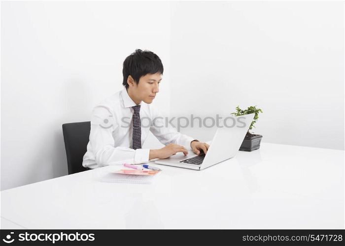 Asian mid adult businessman using laptop at desk in office