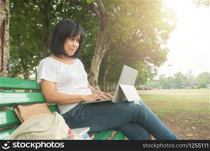 Asian mid adult entrepreneur businesswoman sit in park using laptop for work outside office in casual dress looking notebook with thinking and concentrate in park.