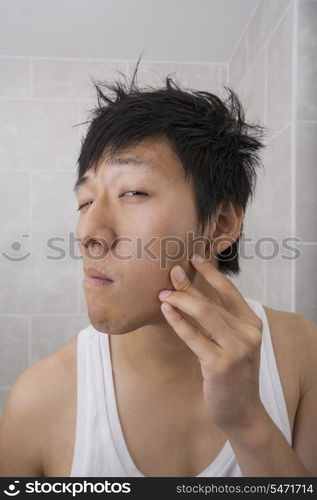 Asian mid adult man examining his face in bathroom