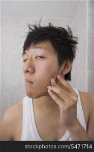 Asian mid adult man examining his face in bathroom
