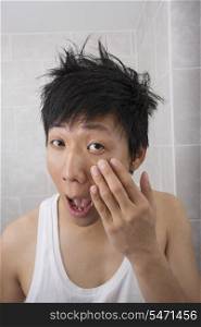 Asian mid adult man inspecting his face in bathroom