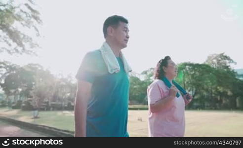 Asian middle age couple taking a walk inside public park, healthy retirement lifestyle, relationship happy family, experienced mature couple warm up exercises, family outdoor relaxing activity