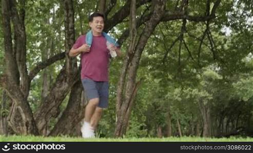 Asian middle age man running and resting at the park, standing under trees and rest after exercising, body wellness tired exhausted, men health care, life insurance plan, work out routine
