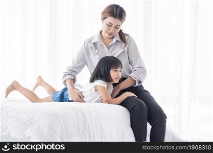Asian mom and her daughter spending happy time in holidays and playing together at home on whit bed