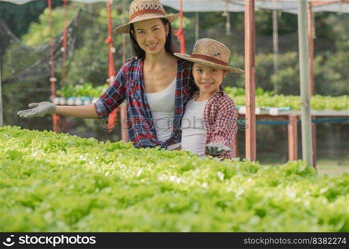 Asian mother and daughter are helping together to collect the fresh hydroponic vegetable in the farm, concept gardening and kid education of household agricultural in family life style.