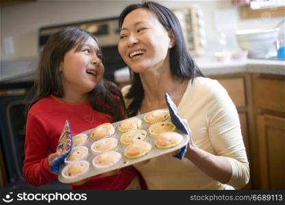 Asian mother and daughter baking muffins in the kitchen at home