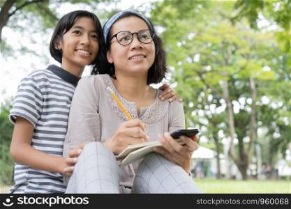 Asian mother and daughter cute are sitting and writing a notebook at public park