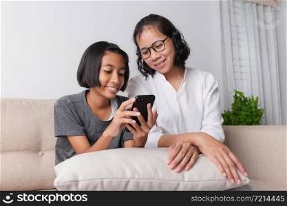 Asian mother and her little daughter using smartphone and smile While sitting on the sofa at home