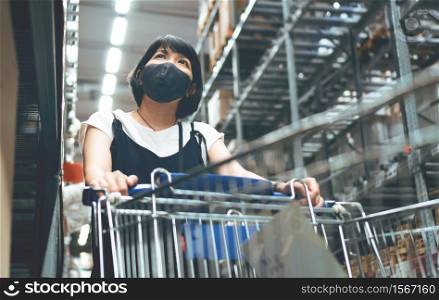 Asian mother buyer wearing protective face mask with shopping cart during pandemic coronavirus at mall while her pregnancy. Young Pregnant Woman looking and selecting products on shelf at supermarket.