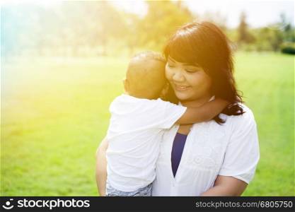 Asian mother carrying and holding her son in green park sunlight. Asian mother carrying and holding her son in green park sunlight.