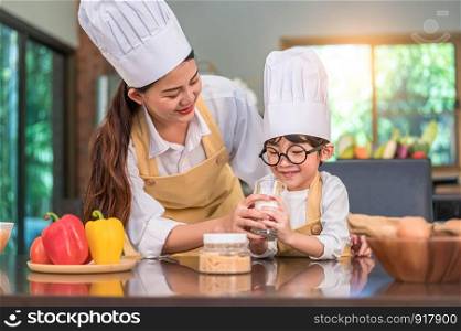 Asian mother helping cute little boy drinking milk in glass at home kitchen in chef cooking uniform. People lifestyles and Happy family togetherness concept. Calcium and protein in milk nutrition