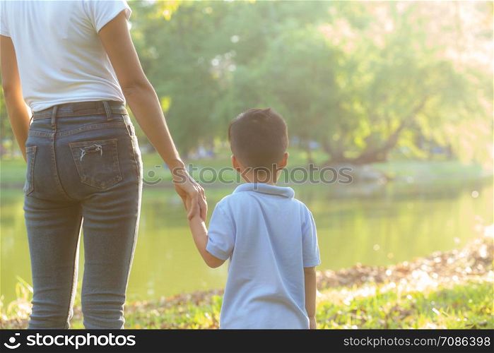 Asian mother or parent and son holding hand with love together in summer outside in the park, mom take care kid holding palm with affection, child have a trust for mother, family concept.