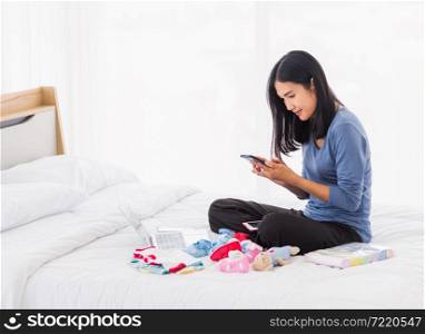 Asian mother shopping online for her baby clothes on laptop computer and tablet on the bed she makes purchase new baby clothes for an unborn baby preparing for the new child