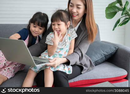 Asian mother with her two grandchildren having fun and playing education games online with a digital computer laptop at home in the living room. Concept of online education and caring from parents.