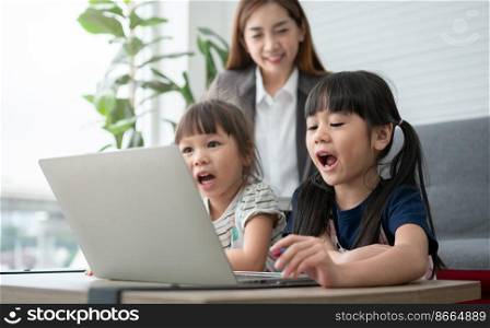 Asian mother with her two grandchildren having fun and playing education games online with a digital computer laptop at home in the living room. Concept of online education and caring from parents.