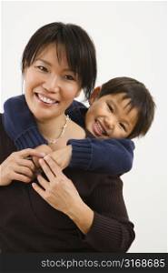 Asian mother with young son hugging her from behind smiling.