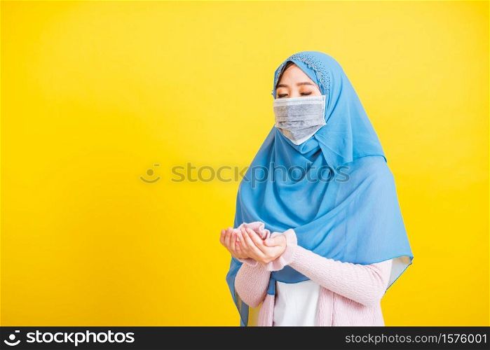 Asian Muslim Arab, Portrait beautiful young woman religious wear veil hijab and face mask protect to prevent coronavirus she henna decorated hands praying to Allah God, isolated on yellow background