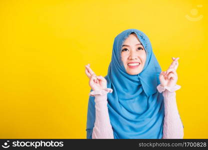 Asian Muslim Arab, Portrait of happy Asian beautiful young woman Islamic religious wear veil hijab she smiling and holding fingers crossed for good luck, studio shot isolated on yellow background