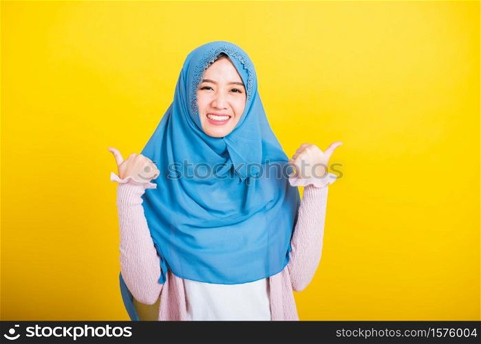 Asian Muslim Arab, Portrait of happy beautiful young woman Islam religious wear veil hijab funny smile she made finger thumbs up, Ok sign to agree, studio shot isolated on yellow background
