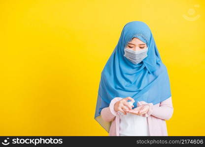 Asian Muslim Arab, Portrait of happy beautiful young woman Islam religious wear veil hijab and face mask protect she quarantines disease coronavirus apply alcohol spray to hands isolated yellow