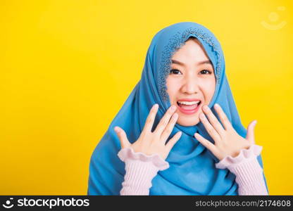 Asian Muslim Arab, Portrait of happy beautiful young woman Islam religious wear veil hijab funny smile she shocking open mouth touching her cheeks with hands isolated yellow background