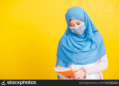 Asian Muslim Arab, Portrait of young woman religious wear veil hijab and face mask protective to prevent coronavirus she student hold books on hand, isolated on yellow background, Back to college