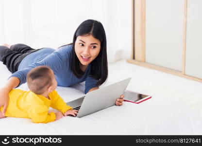 Asian new young beautiful mother finding and reads information on a laptop for milk mixing on a bottle in the bedroom at home