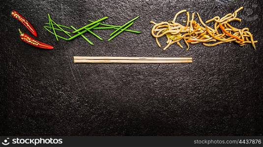 Asian noodles with chopstick, red chili ,chopped chives on black slate background, top view, banner for website