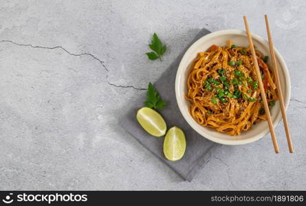 Asian noodles with vegetables and coconut milk on the linen napkin. Light background with lime and bamboo chopsticks.