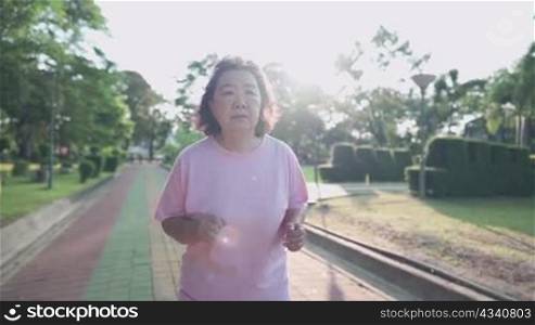 Asian obese old woman jogging inside the park on a sunny morning, Retirement healthy life activity. Elderly Health care, calories diet control, over weight lady running, fight cancer, encourage people