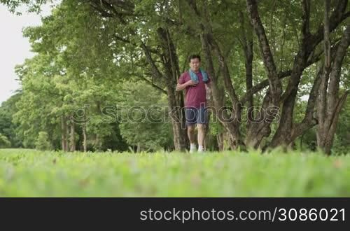 Asian old age man stop and resting during running at the park, standing under trees and rest after exercising, body wellness tired exhausted, men heath, elderly retired life, afternoon cardio wortout